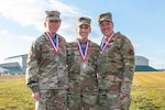 Three women stand together outside in military uniform wearing race medals around thier necks.