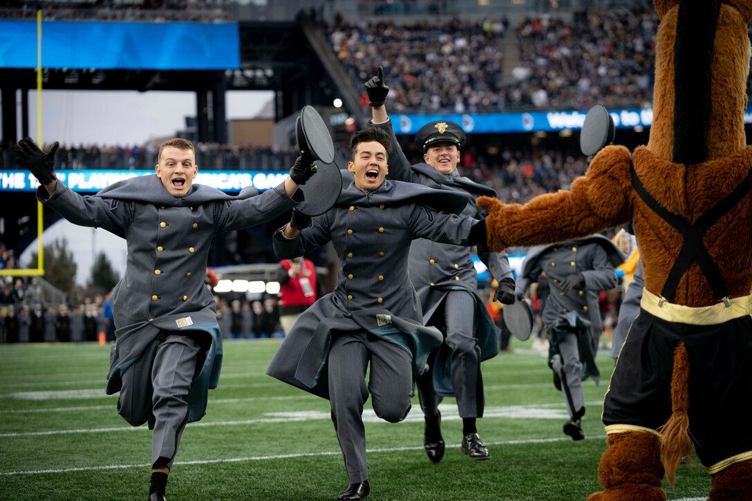 U.S. Military Academy cadets cheer while running on a football field.