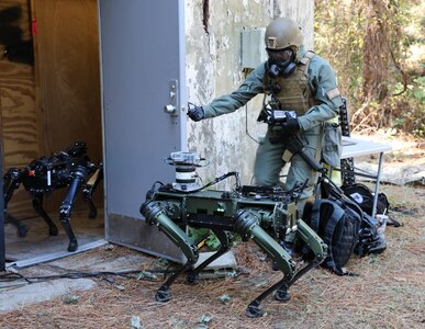CBRN sensors on robot dogs are let into a door by a service member in full CBRN gear.