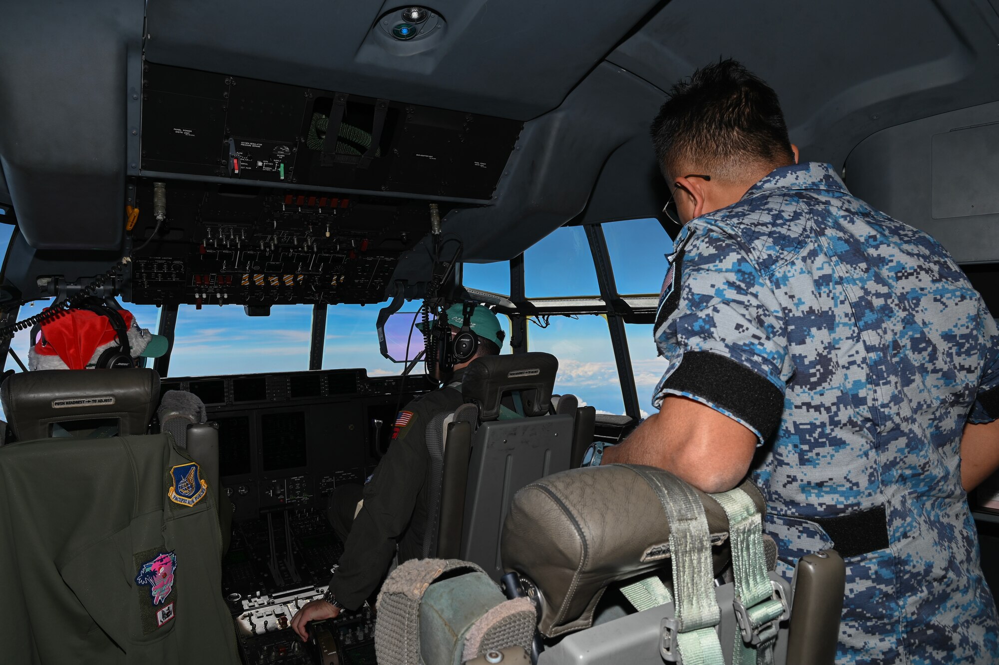 Two U.S. Air Force Airmen pilots and a Royal Malaysian Air Force Airman view the horizon inside the cockpit of a USAF C-130J Super Hercules