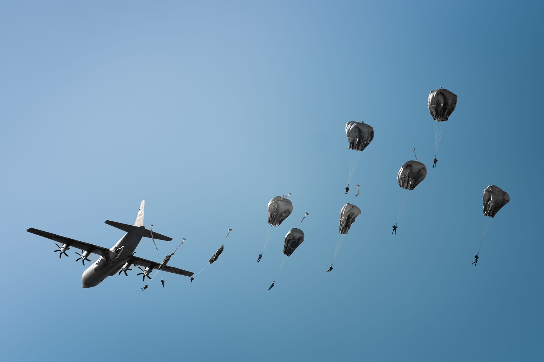 Paratroopers deploy their parachutes near an aircraft flying in blue sky.