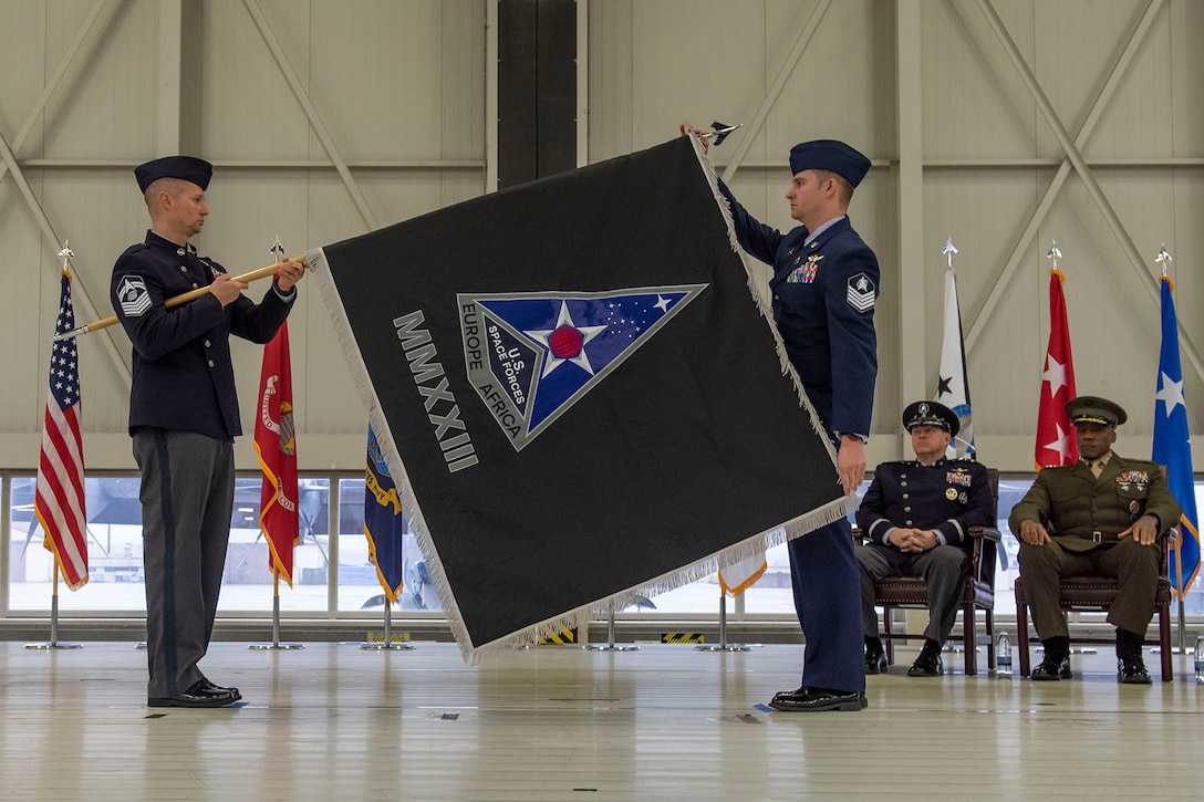 Two airmen hold a flag as it is unfurled.