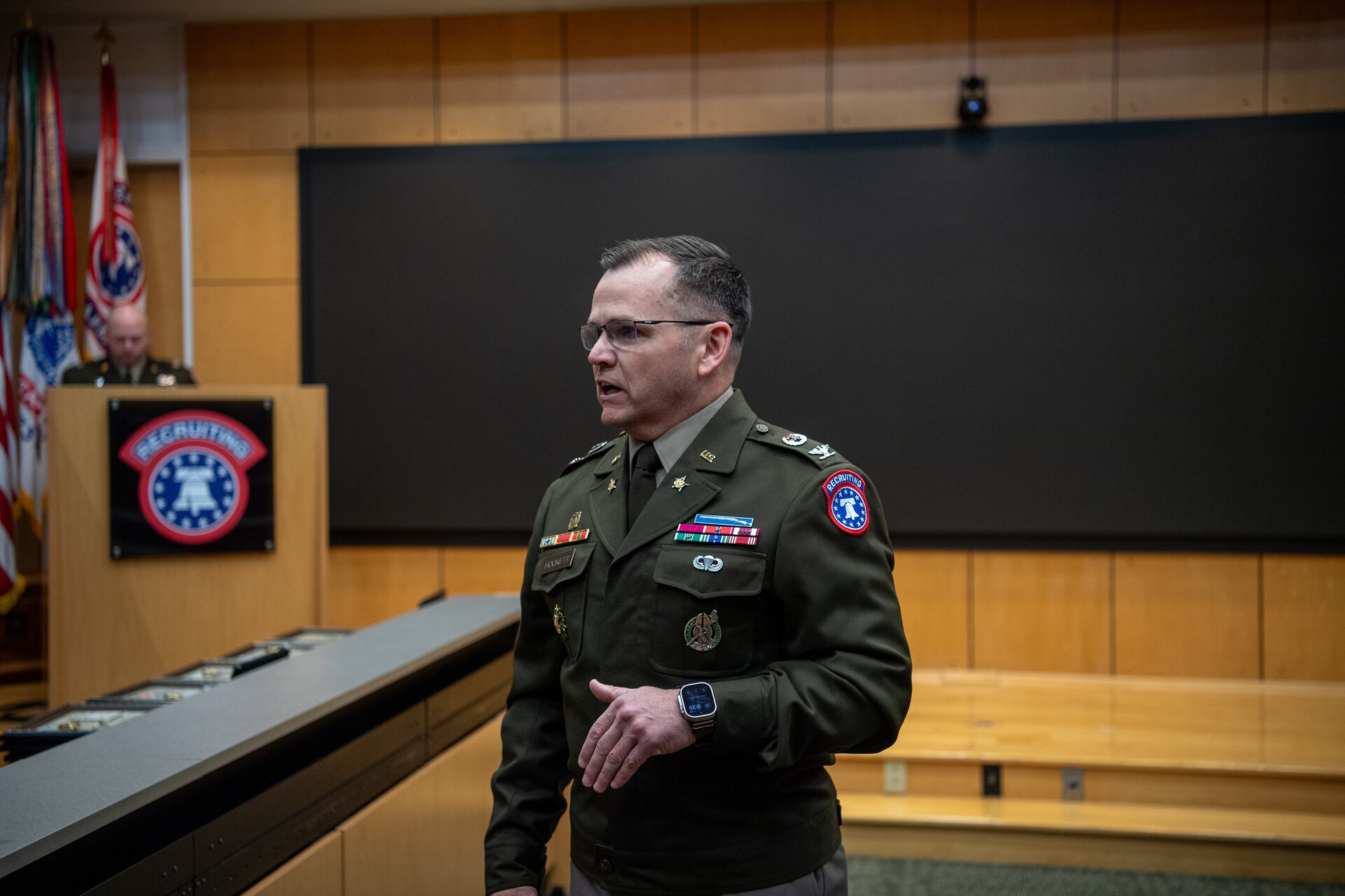 A male U.S. Army Soldier in dress uniform stands to give remarks during an award ceremony.