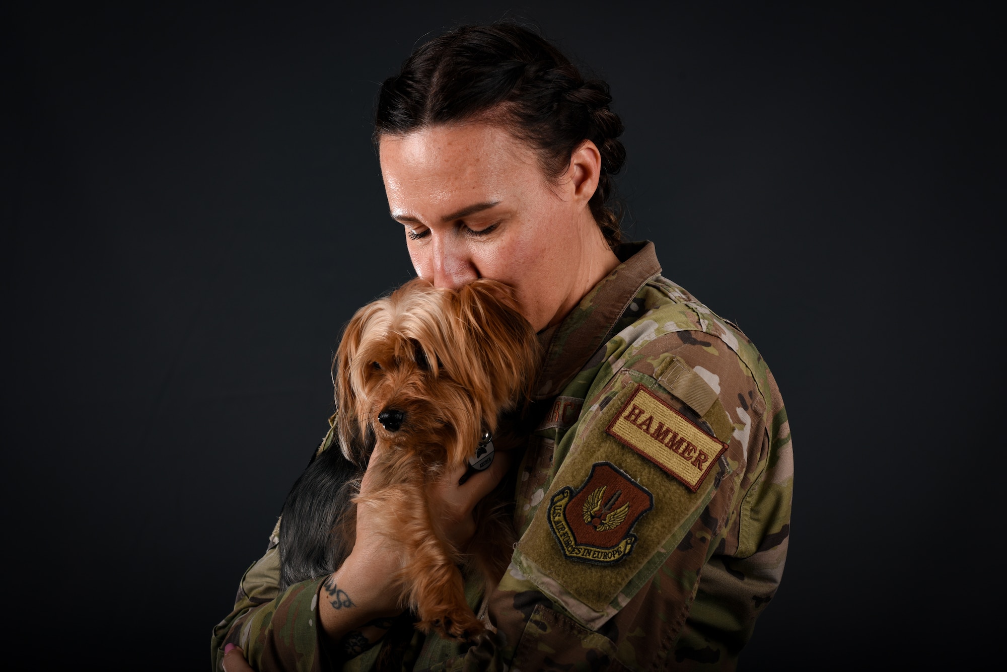 A woman in uniform holds a small dog and kisses the back of its head.