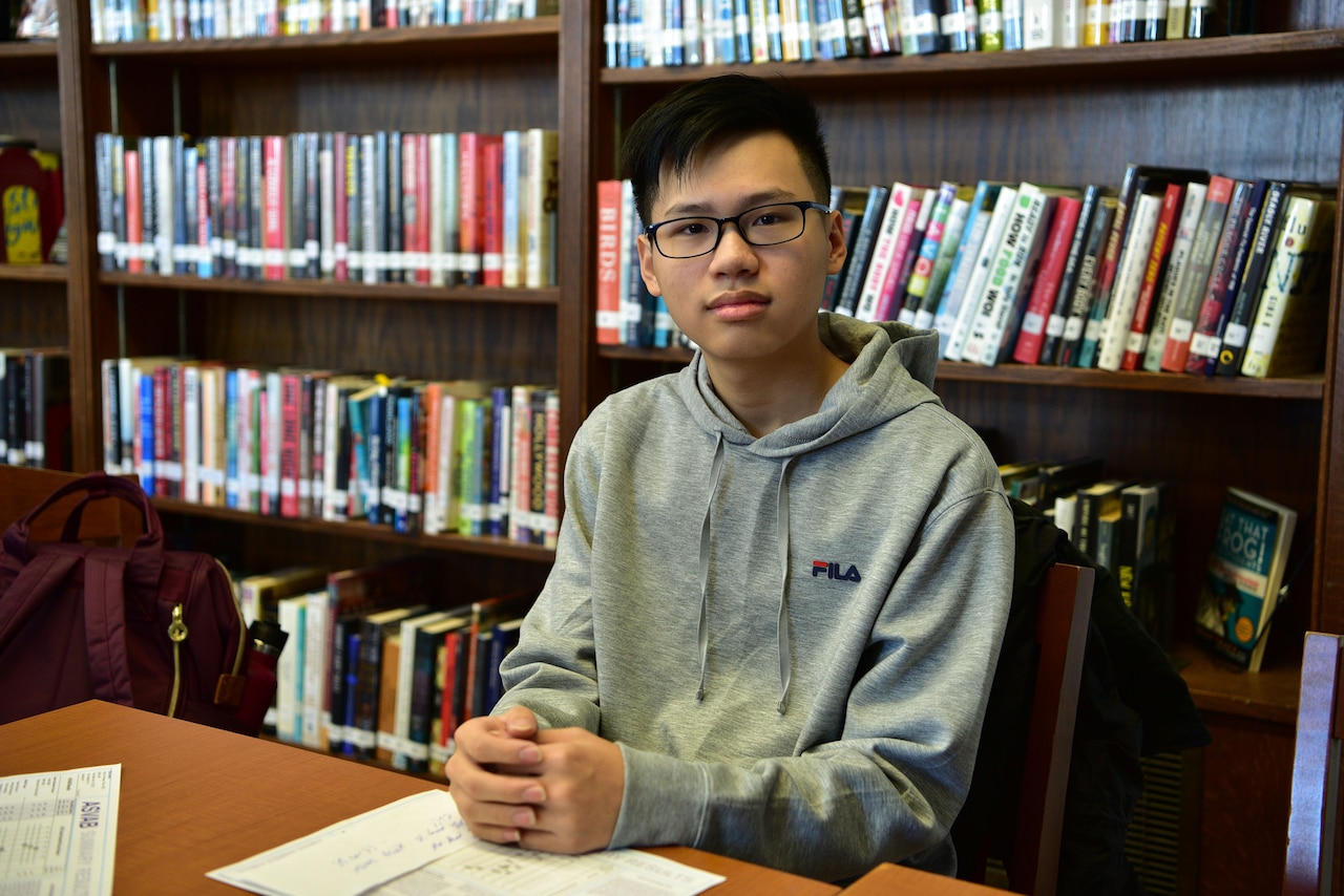 A student is seated at a table near a bookshelf.