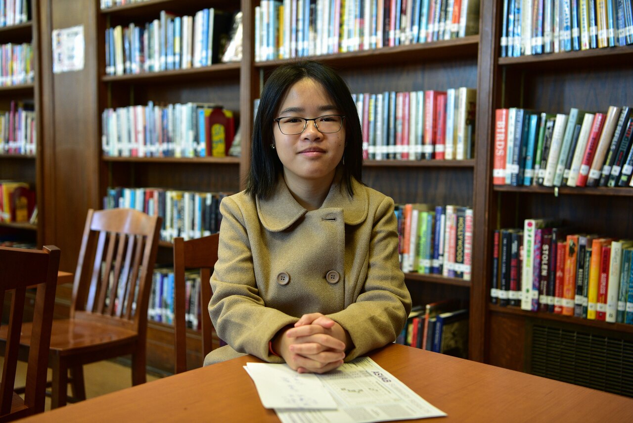 A student is seated at a table near a bookshelf.