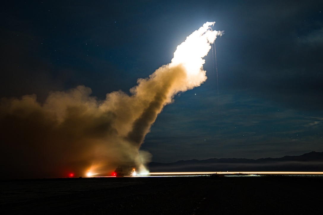 A rocket system is fired at night leaving a trail of smoke in the sky.