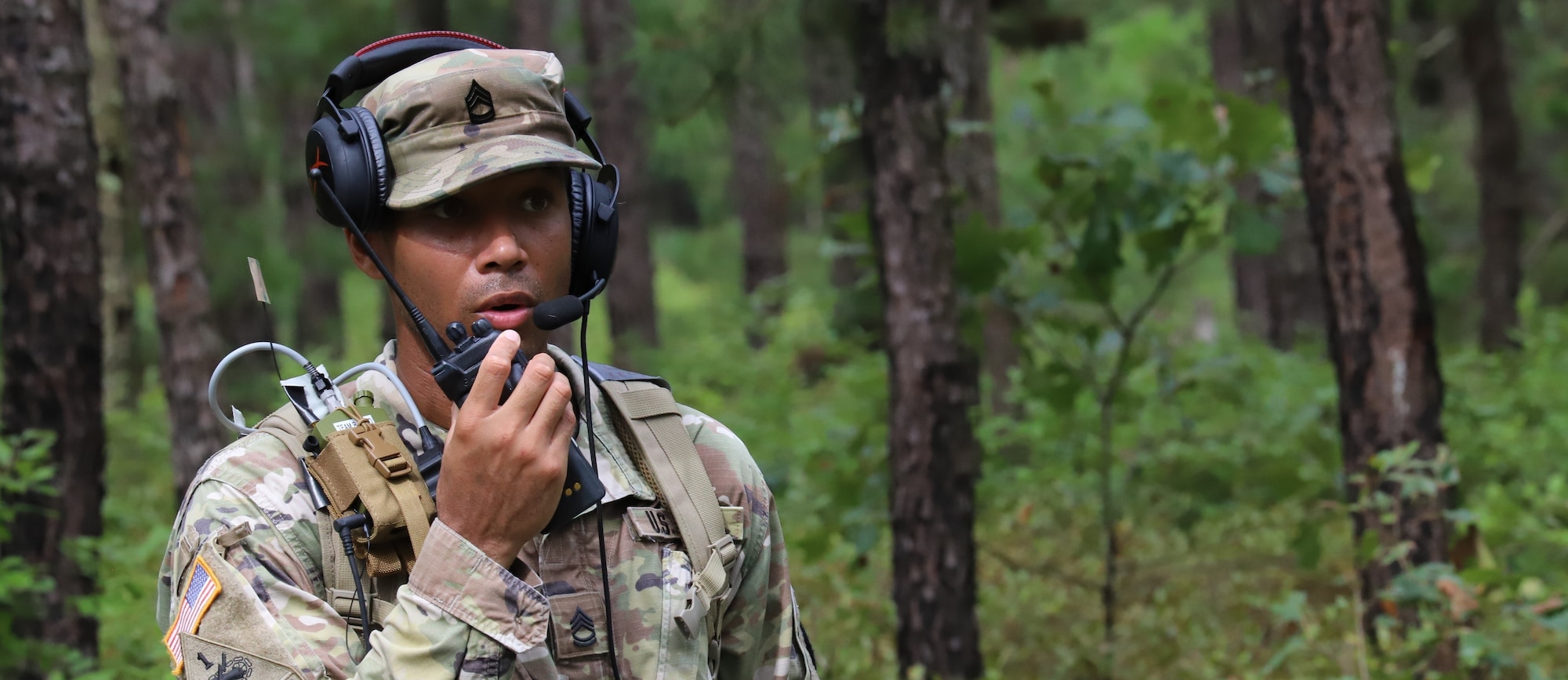Soldier talks into a radio in a wooded area on JB-MDL.