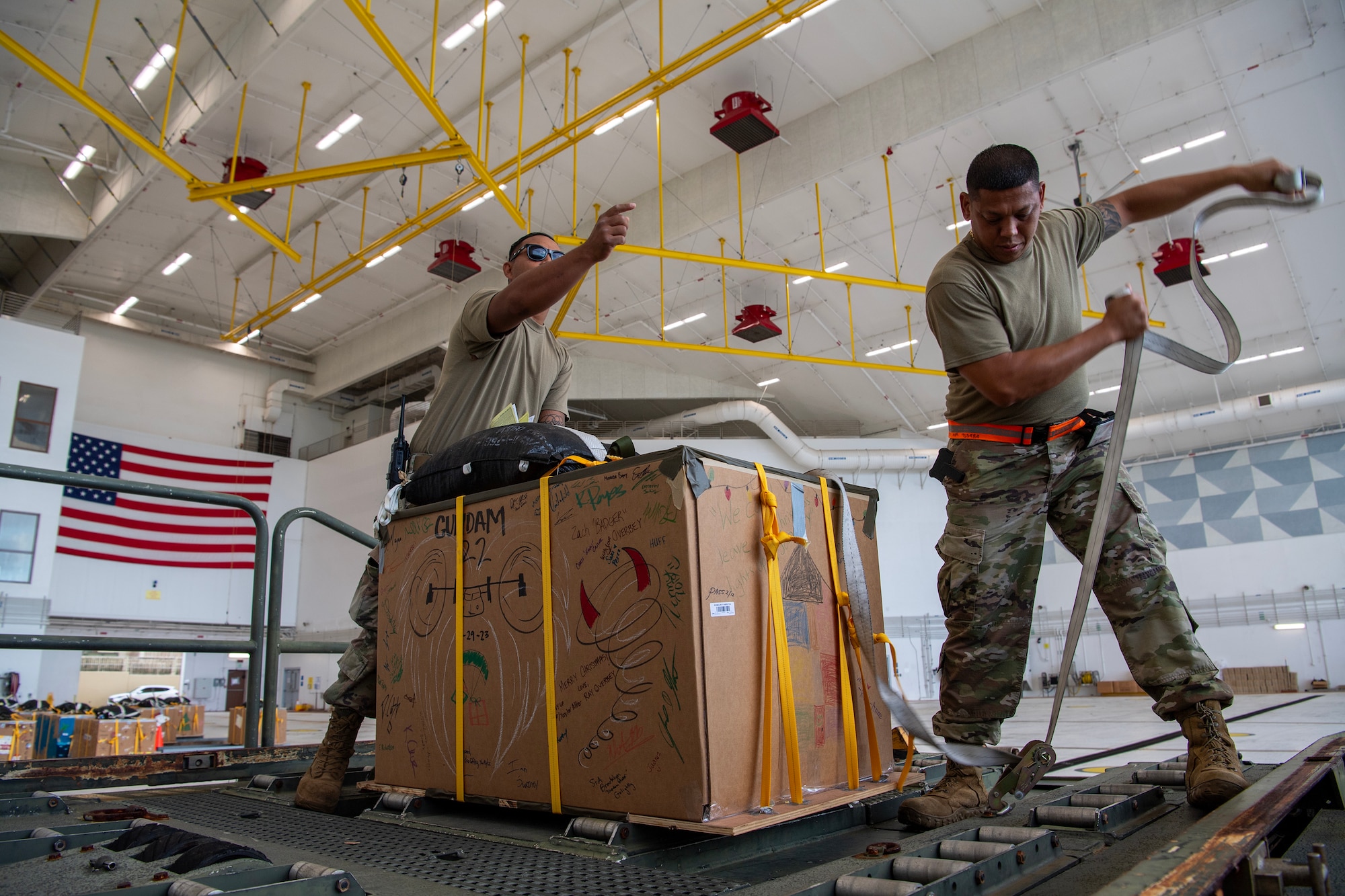 Photo of U.S. Air Force aerial port Airmen securing an Operation Christmas Drop 2023 bundle for loading.