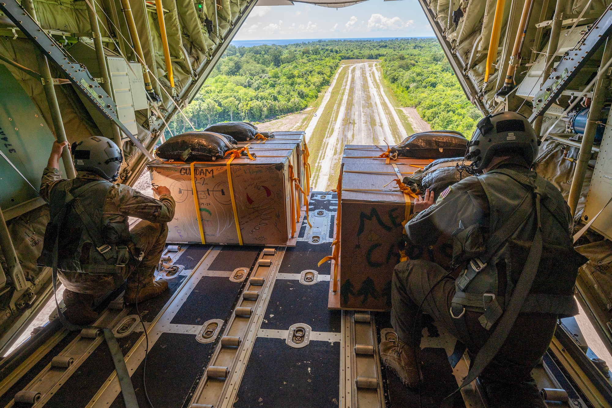 Photo of U.S. Air Force loadmasters pushing Operation Christmas Drop 2023 bundles from a C-130J