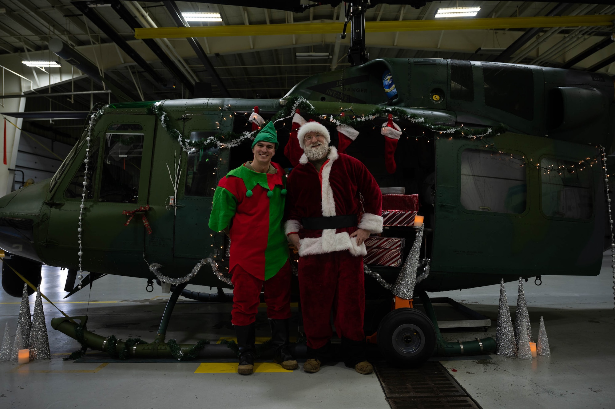 Santa Claus and an elf pose for a photo during the 54th Helicopter Squadron (HS) holiday party at Minot Air Force Base, North Dakota on December 10, 2023. At the HS holiday party, Claus takes the time to meet with children and pose for photos with members of Team Minot. (U.S. Air Force photo by A1C Luis Gomez)