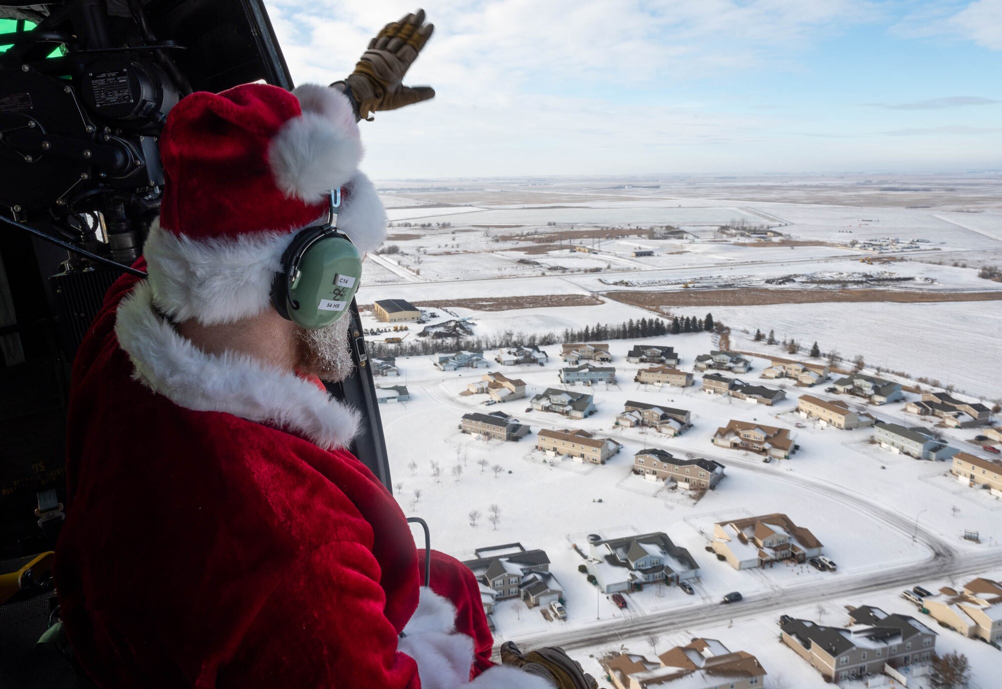 Santa Claus waves to families as he flies in a UH-1N Iroquois at Minot Air Force Base, North Dakota on December 10, 2023. Every year Claus and his elf crew greet the children of Minot Air Force Base and Minot, N.D. from the sky. (U.S. Air Force photo by A1C Luis Gomez)