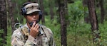 Soldier talks into a radio in a wooded area on JB-MDL.