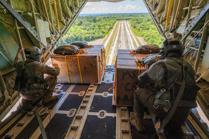 Photo of U.S. Air Force loadmasters pushing Operation Christmas Drop 2023 bundles from a C-130J