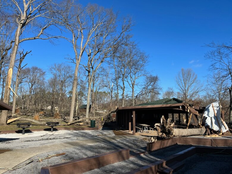 Outdoor pavilion with damage to it, and downed trees around it.