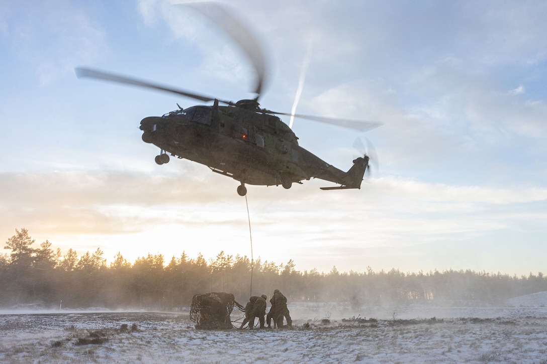 Marines conduct a sling load exercise during on a snowy landscape.