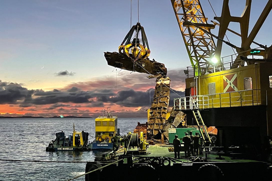 A  portion of a sunken ship is lifted by a crane.