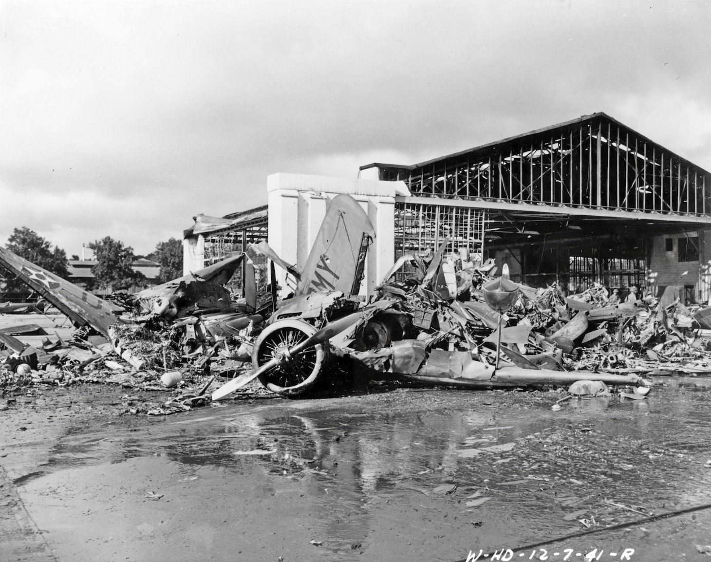 U.S. Army aircraft destroyed by Japanese raiders at Wheeler Air Field. Photographed later in the day on 7 December 1941, following the end of the attacks. Wreckage includes at least one P-40 and a twin-engine amphibian. Note the wrecked hangar in the background.
