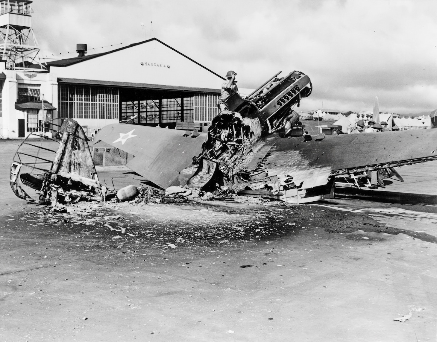 Men examine the burned-out wreckage of a P-40 fighter, possibly from the 78th Pursuit Squadron near Hangar 4 at Wheeler Air Field, following the end of the Japanese raid. Note the long blast tubes for the aircraft’s two .50-caliber nose machine guns. The early P-40s also had four wing-mounted .30-caliber machine guns. Before the raid, there were 99 P-40s available from various squadrons around the several bases. By day’s end, only 27 remained operational.