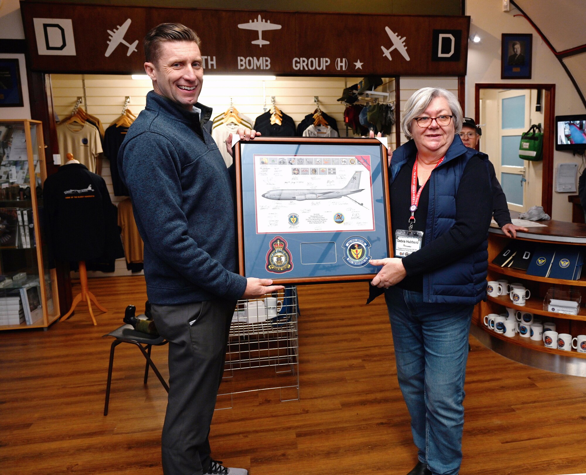 U.S. Air Force Col. Ryan Garlow, 100th Air Refueling Wing commander, left, presents a lithograph of a KC-135 Stratotanker to Debra Hubbard, 100th Bomb Group Memorial Museum chair of trustees, at Thorpe Abbotts, Norfolk, England, Dec. 4, 2023. Base leadership from Royal Air Force Mildenhall spent time at the museum for an off-site meeting, followed by a tour to learn more about the heritage of the 100th ARW. (U.S. Air Force photo by Karen Abeyasekere)