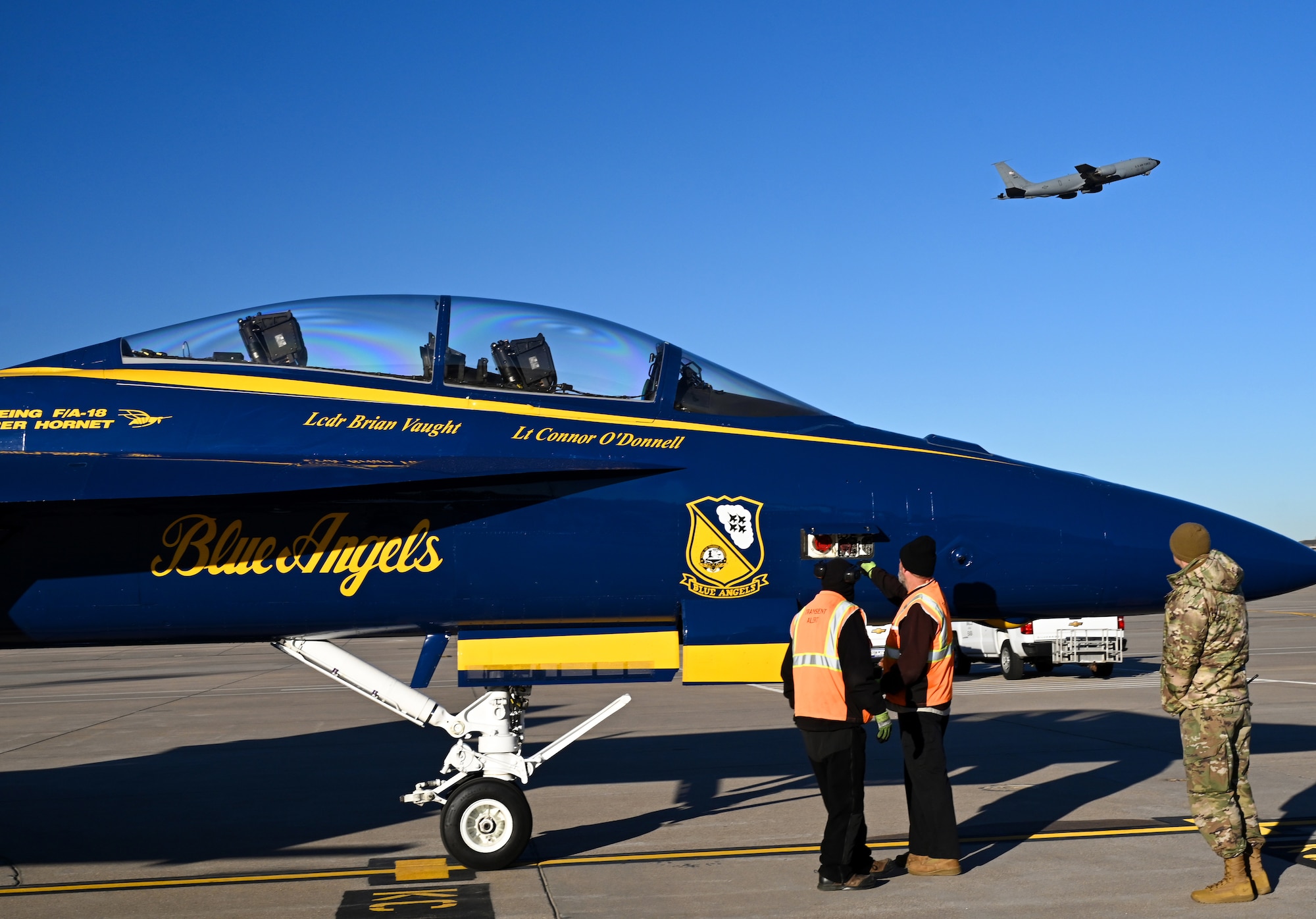 Members of the 22nd Logistics Readiness Squadron prepare to refuel a U.S. Navy F/A-18 Super Hornet belonging to the U.S. Navy Flight Demonstration Squadron, the Blue Angels, while a U.S. Air Force KC-46A Pegasus takes off Dec. 11, 2023, at McConnell Air Force Base, Kansas Two Blue Angels visited McConnell in preparation for their part in the Frontiers in Flight Air Show on Aug. 24-25, 2024. (U.S. Air Force photo by Staff Sgt. Tryphena Mayhugh)