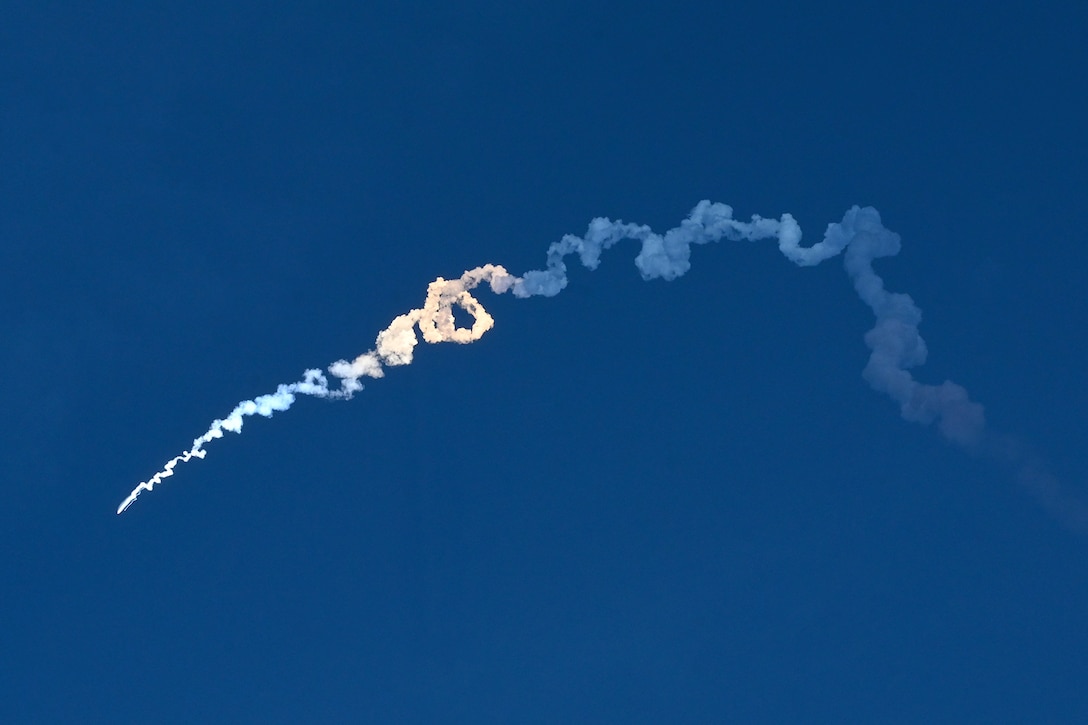 A missile launches creating a trail of smoke against a deep blue sky.