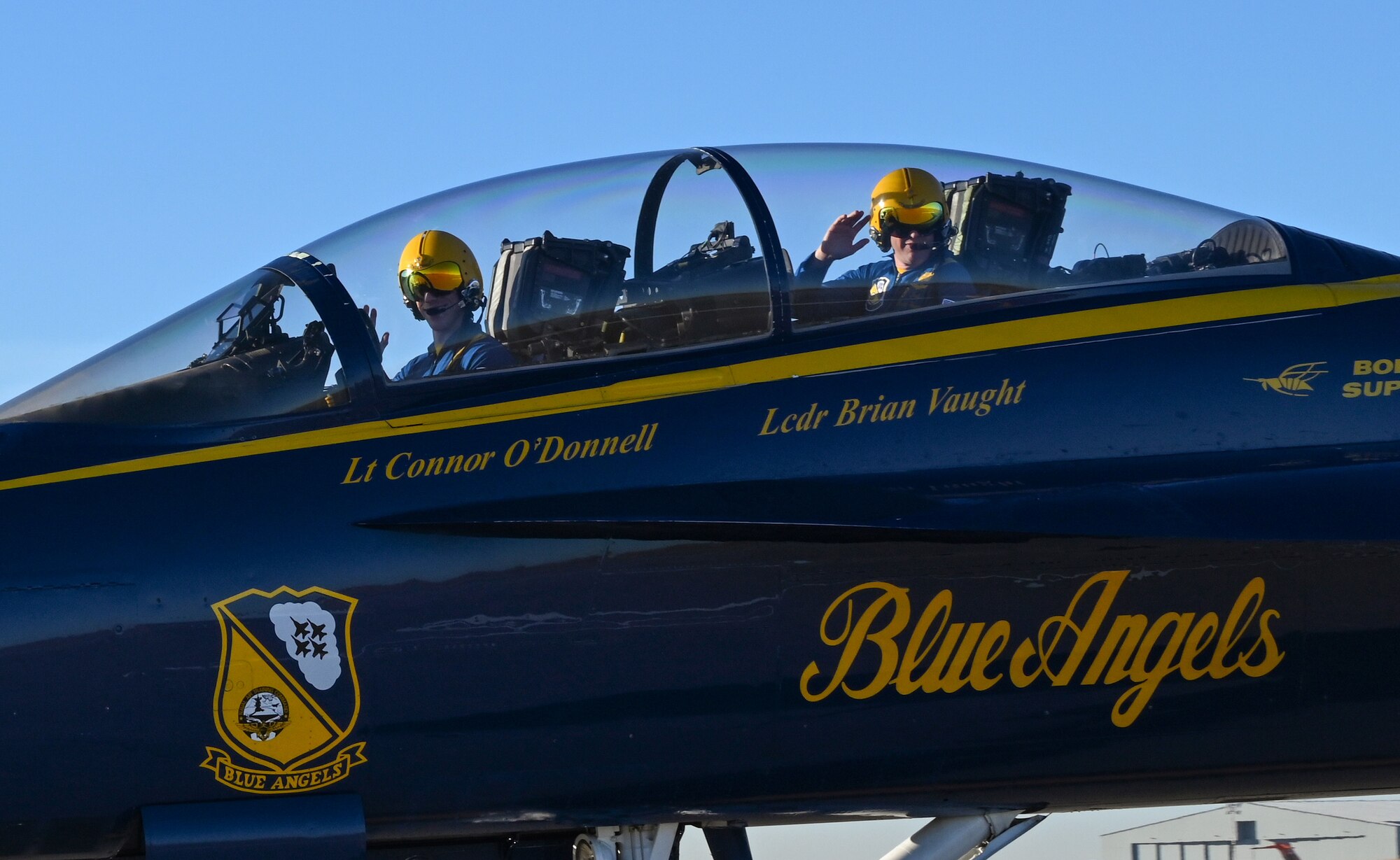 U.S. Navy Flight Demonstration Squadron, the Blue Angels, narrator Navy Lt. Connor O’Donnell, left, and event coordinator Navy Lt. Cmdr. Brian Vaught, wave as they taxi to their parking spot Dec. 11, 2023, at McConnell Air Force Base, Kansas. The two Blue Angels visited McConnell in preparation for their part in the Frontiers in Flight Air Show on Aug. 24-25, 2024. (U.S. Air Force photo by Staff Sgt. Tryphena Mayhugh)