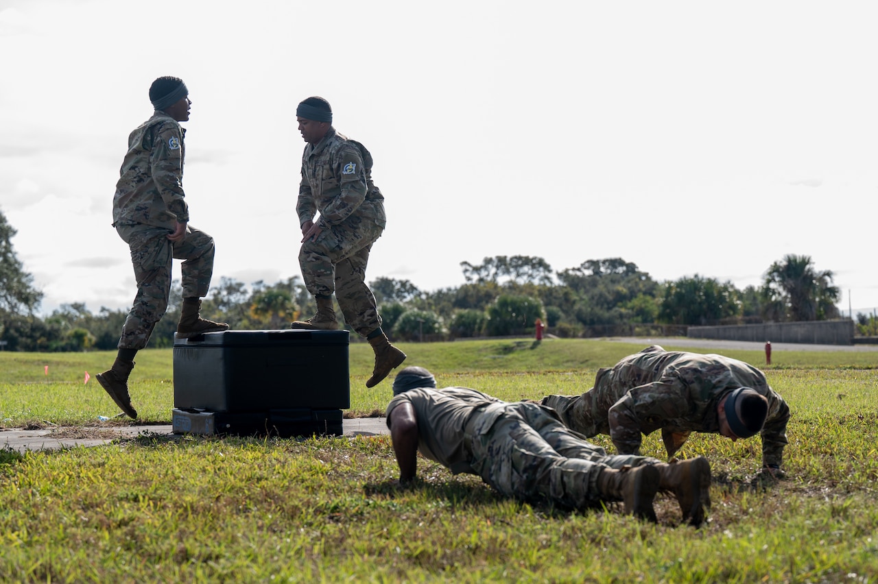 Two guardians perform pushups while two other guardians climb a box.