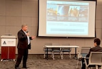 Man speaks in front of presentation screen.