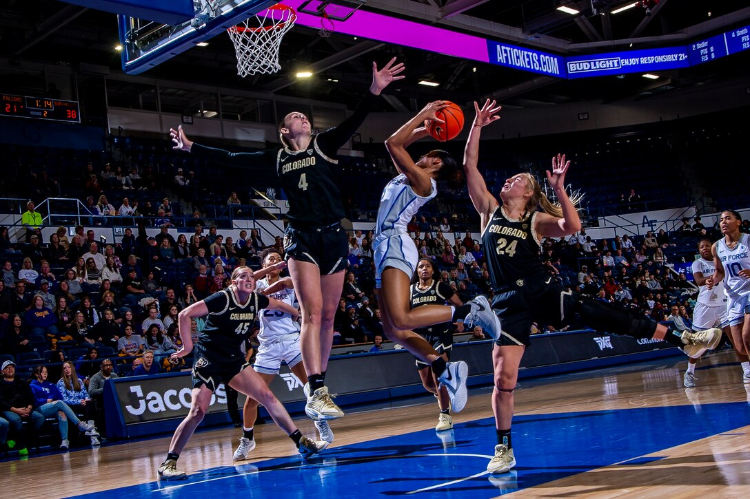 A basketball player shoots a jump shot between two defenders.