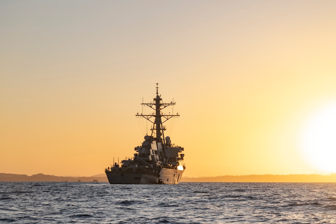 A military ship sails at sunset.