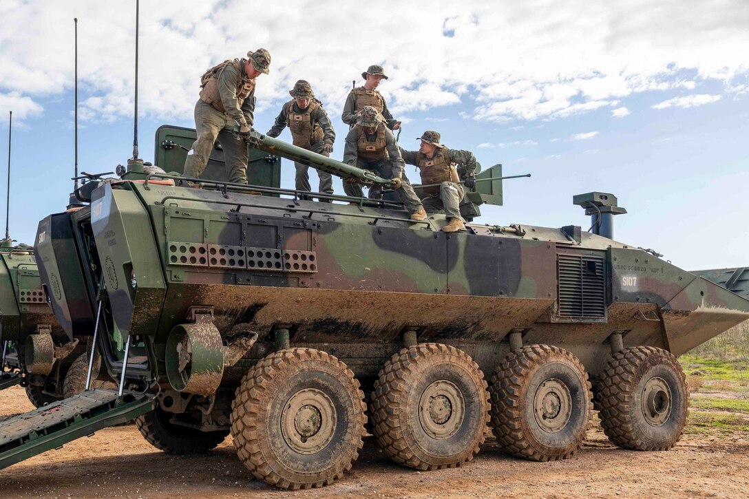 Marines move equipment on top of a military vehicle.