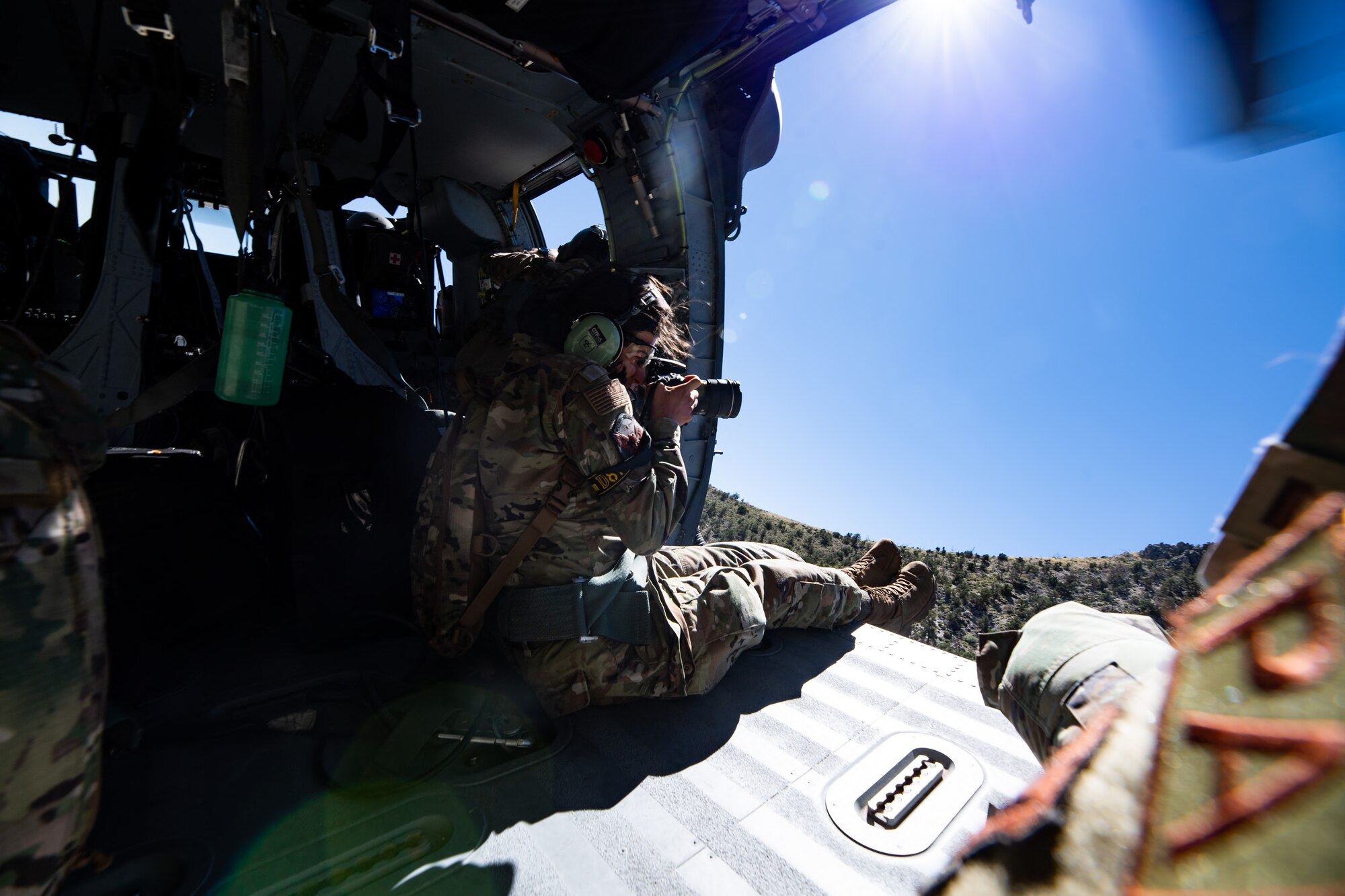 An airman takes a photo from a helicopter.