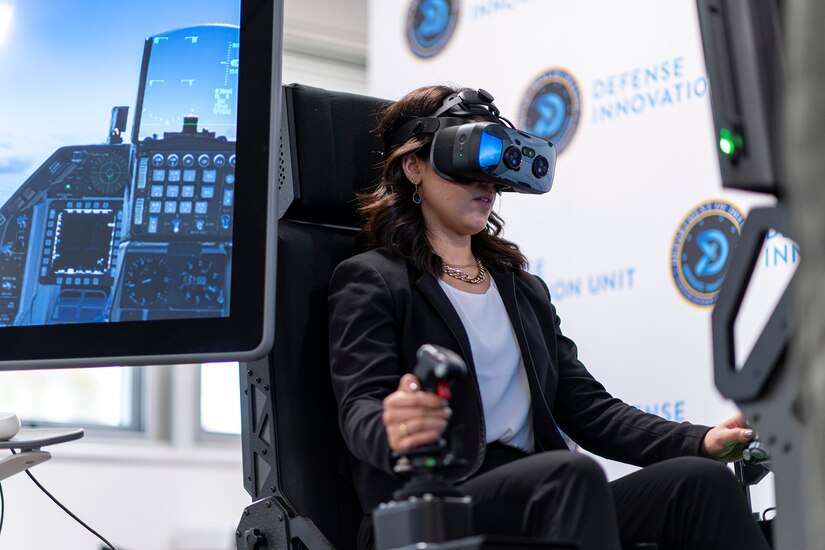 A person sits in a video gaming chair while wearing virtual reality goggles.