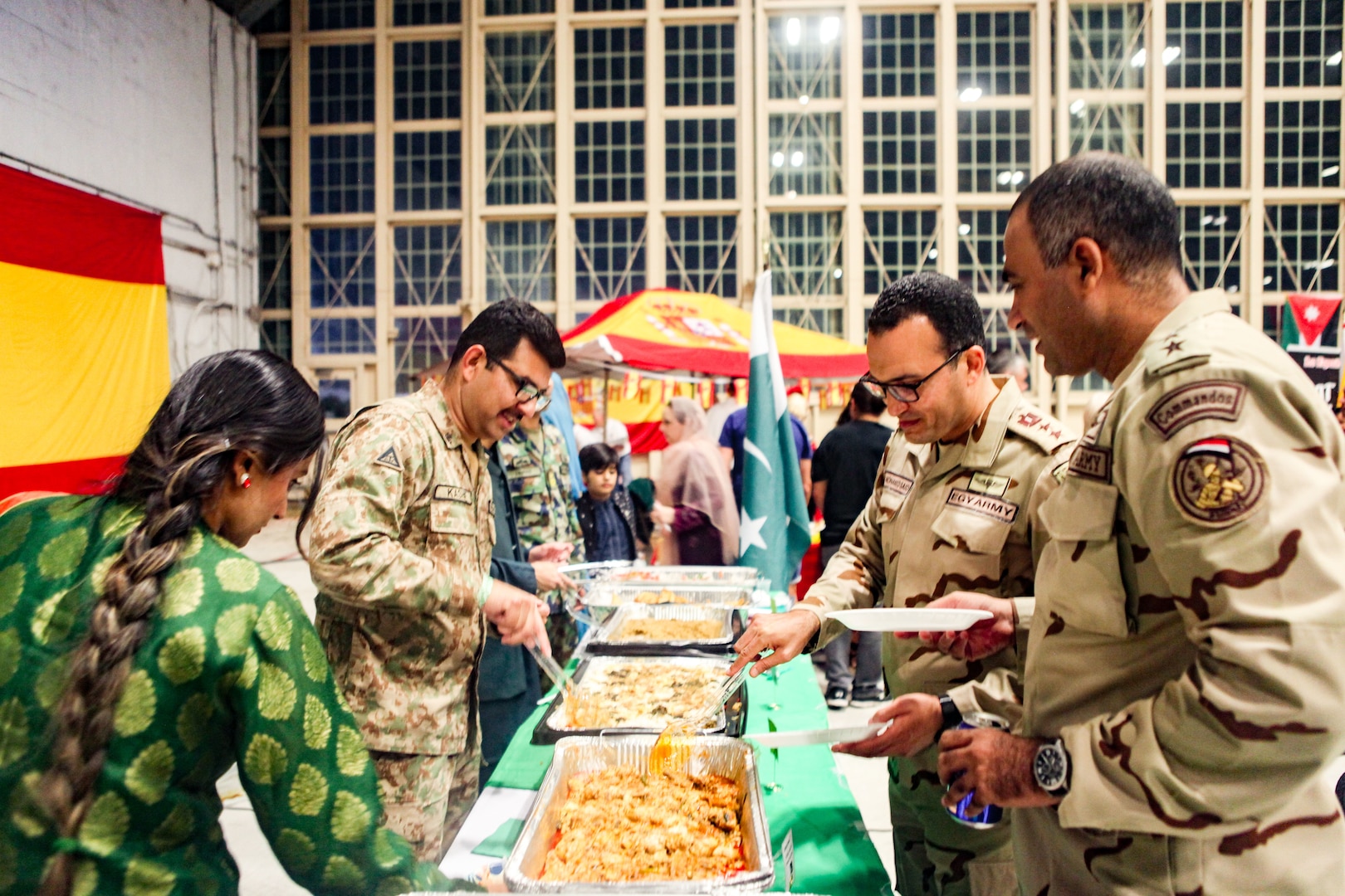 TAMPA, Fla. - Two Egyptian officers (right) sample Pakistani food during U.S. Central Command’s (CENTCOM) International Night, Dec. 07, 2023. International Night started in December 2004 as a winter holiday party for the Coalition members and families. This year, members of CENTCOM’s coalition countries displayed native customs and offered a taste of their traditional cuisines to guests. (U.S. Central Command Public Affairs photo by Maged Benjamin-Elias)