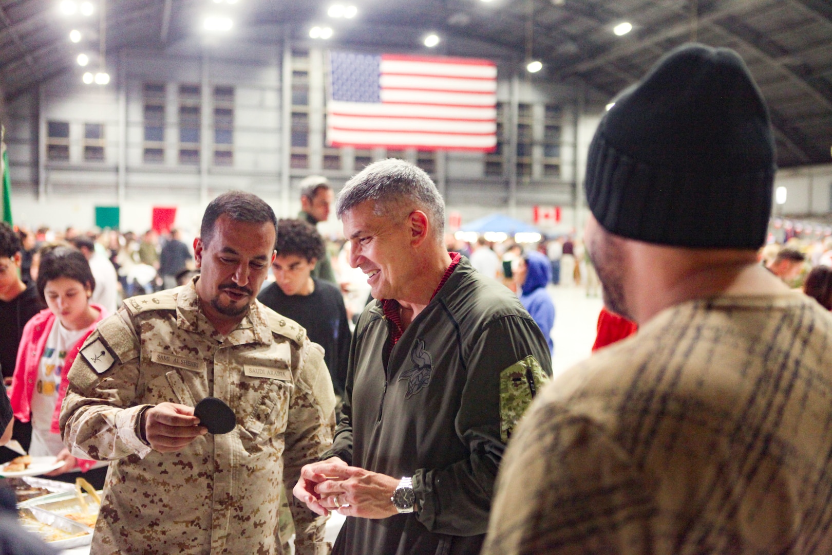 TAMPA, Fla. – A Saudi Senior National Representative (left) shows off an item during U.S. Central Command’s (CENTCOM) International Night, Dec. 07, 2023. International Night started in December 2004 as a winter holiday party for the Coalition members and families. This year, members of CENTCOM’s coalition countries displayed native customs and offered a taste of their traditional cuisines to guests. (U.S. Central Command Public Affairs photo by Maged Benjamin-Elias)