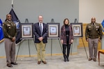 two men in uniform, a civilian man and civilian woman pose next to plaques on stands