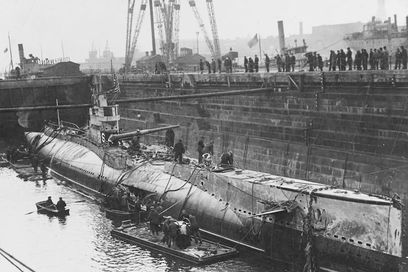 A damaged submarine sits on the water at a dock.