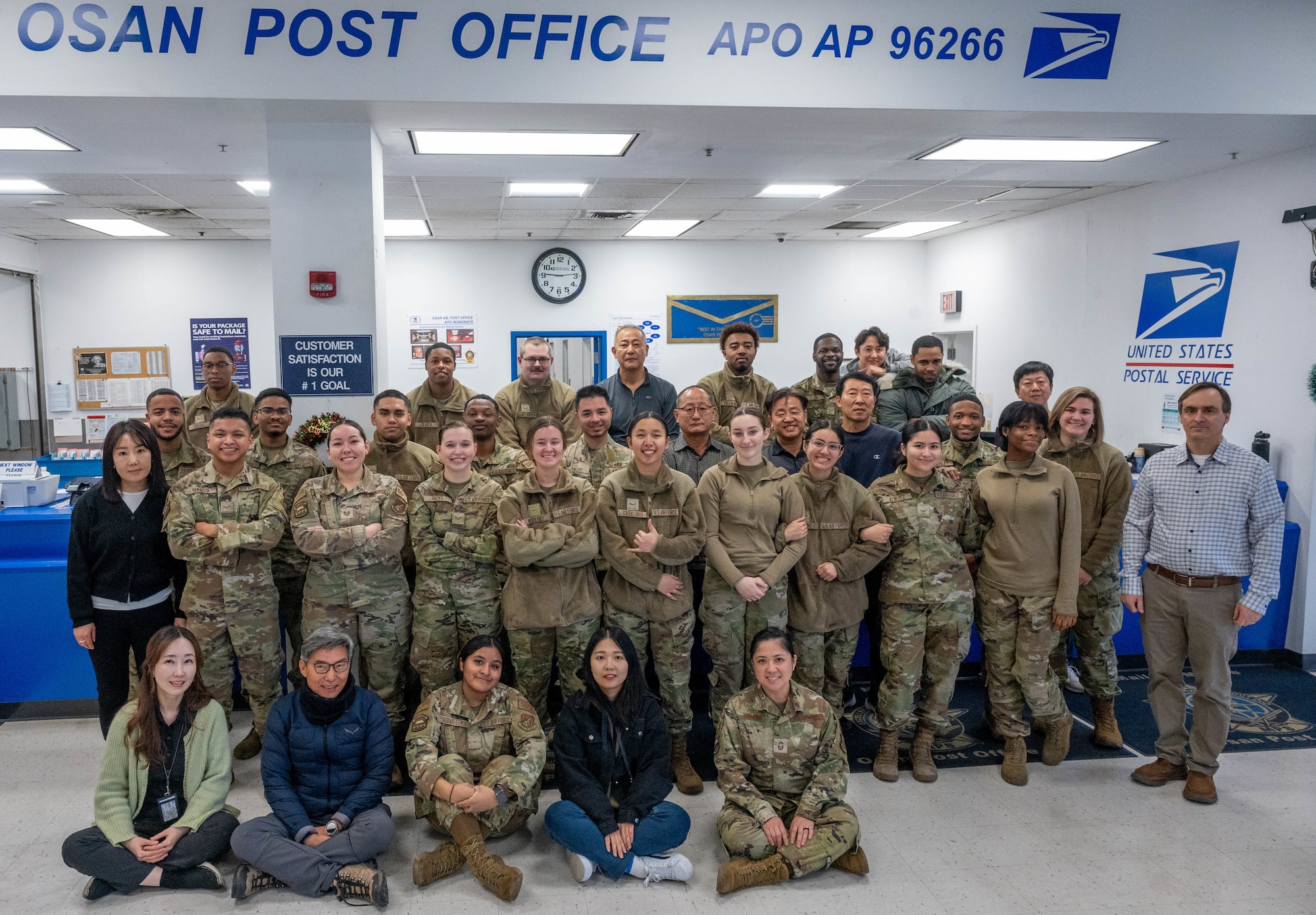 Members from the Osan Air Base Post Office pose for a group photo at Osan Air Base, Dec. 12, 2023. The base post office operates with a total of 40 personnel, including 28 military, 12 Korean Nationals, and one GS civilian to handle all of the incoming and outgoing mail for the base. The post office provides numerous options to the Airmen on base who might need specific services like placing mail on hold while away or appointing someone trusted to pick up mail on their behalf. (U.S. Air Force photo by Airman 1st Class Chase Verzaal)