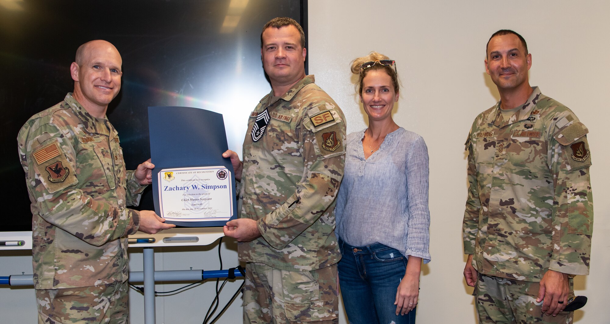 Three U.S. Air Force service members, A Chief Master Sergeant select and his spouse, pose with a certificate.