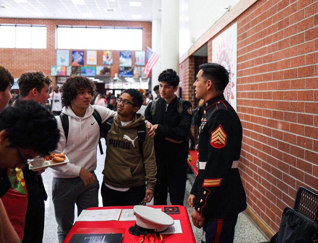 U.S. Marine Corps Sgt. Jorge Salinas, right, a recruiter with Recruiting Substation Virginia Beach, Recruiting Station Richmond, 4th Marine Corps District, speaks with students about Marine Corps opportunities during a high school visit at Salem High School in Virginia Beach, Virginia, Nov. 15, 2023. Salinas invited the attendees to the display and passed out t-shirts to further connect with the local student population and raise Marine Corps awareness. (U.S. Marine Corps photo by Sgt. Godfrey Ampong)