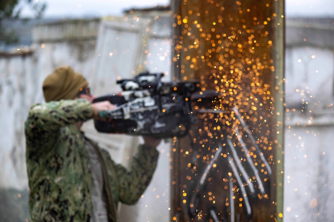 A service member uses a cutting tool to breach a wall during training.