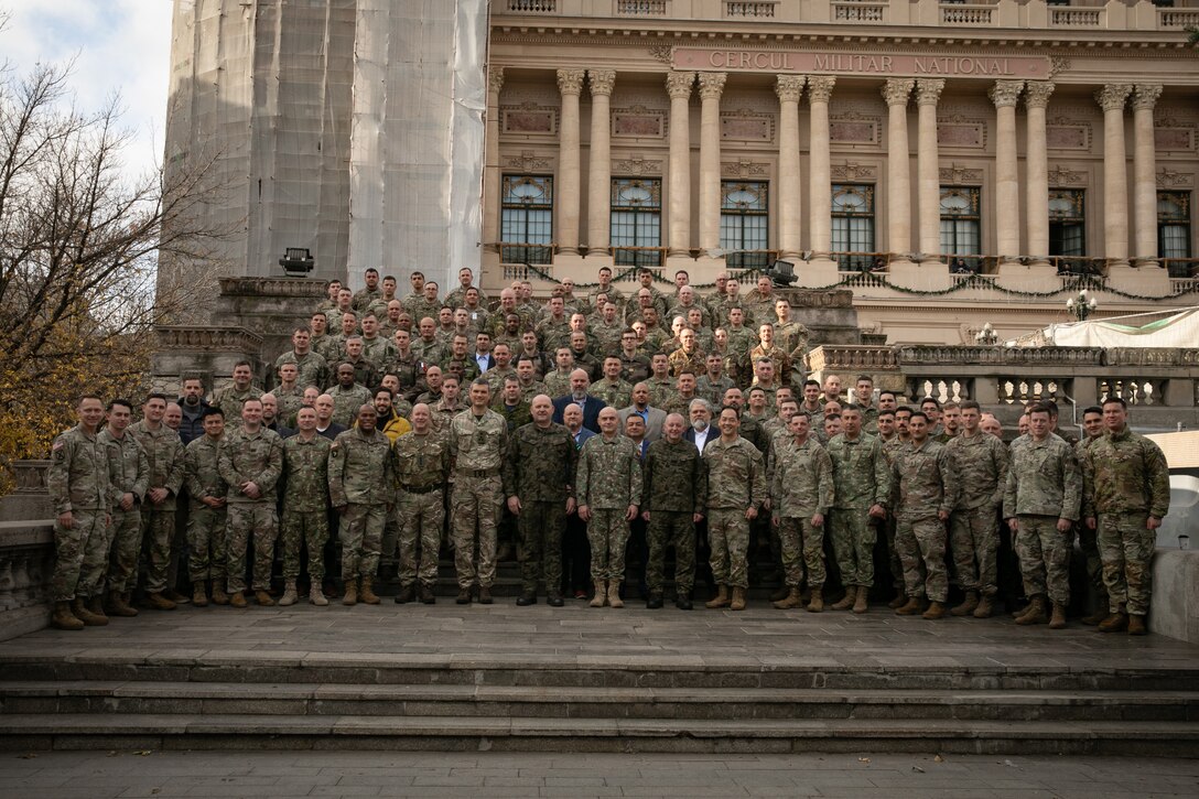 U.S., Romania, Italy, France, Lithuania, Estonia, Poland, and Great Britain service members pose for a group photo during the European High Mobility Artillery Rocket System Initiative III Summit in Bucharest, Romania, Dec. 6, 2023. U.S. Army V Corps troops worked alongside NATO partner forces to host the event, in which field artillery experts of different nations discussed HIMARS capabilities that enforce readiness and interoperability between the U.S. and partner forces. (U.S. Army Reserve photo by Spc. Devin McReynolds)