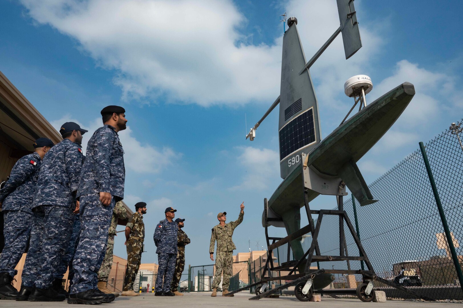 Members of U.S. and foreign militaries observe an unmanned naval vessel ashore.