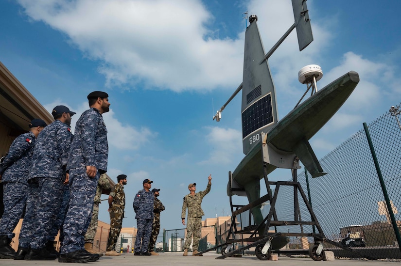 Members of U.S. and foreign militaries observe an unmanned naval vessel ashore.