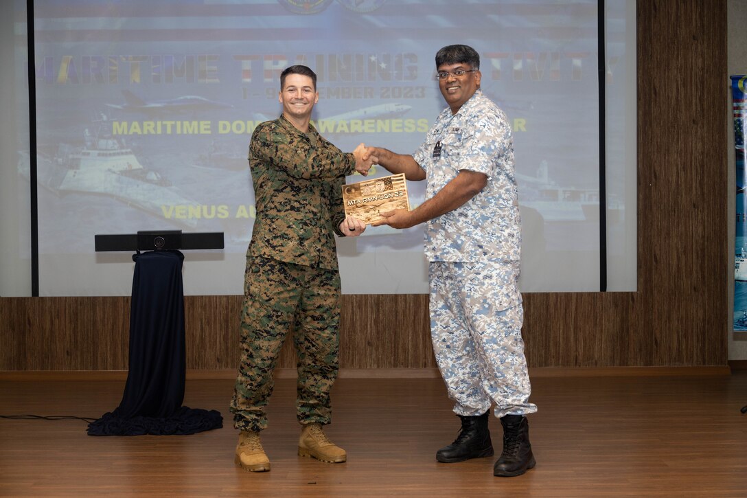 Royal Malaysian Navy sailor Cdr. John Gomez, right, a maritime intelligence staff officer with Western Fleet Command, presents a gift to U.S. Marine Corps Capt. Philip Badrov, exercise force officer-in-charge with Marine Rotational Force-Southeast Asia, I Marine Expeditionary Force, during a Maritime Domain Awareness subject matter expert exchange at Maritime Training Activity Malaysia 2023 at Lumut Naval Base, Lumut, Malaysia, Nov. 2, 2023. The exchange focused on applying both MDA and Expeditionary Advanced Base Operations to achieve a littoral advantage. MTA Malaysia 2023 highlights the 4th iteration of the exercise as one of many exercises that allow the U.S. and Royal Malaysian navies to work together, enhancing maritime security and capabilities in the full range of maritime warfare. MRF-SEA is a Marine Corps Forces Pacific operational model, which involves planned exchanges with subject matter experts, promotes security goals with Allies and partners and positions I MEF forces west of the International Date Line. (U.S. Marine Corps photo by Staff Sgt. Kai W. Huber)