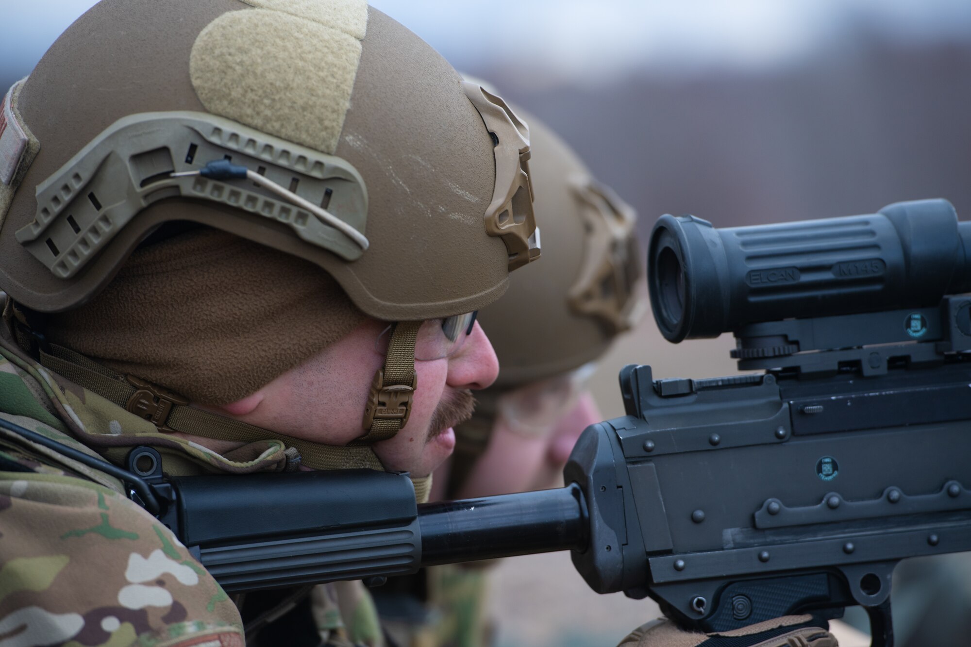 Man peers through scope of machine gun.