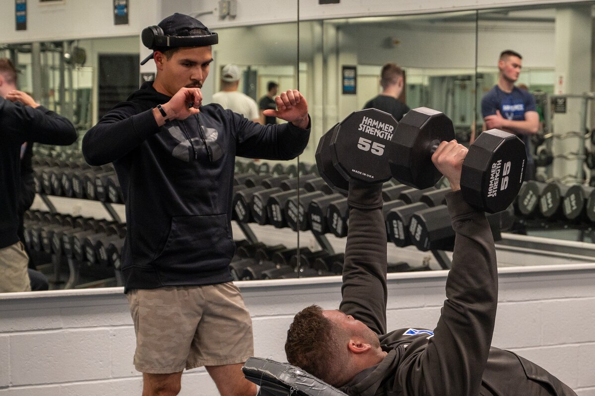 U.S. Air Force Maj. Miles Stutes, 354th Medical Group Operational Support Team physical therapist (right) demonstrates correct form to Senior Airman Ricardo Siqueiros, 354th Security Forces Squadron military working dog handler during a group physical training session