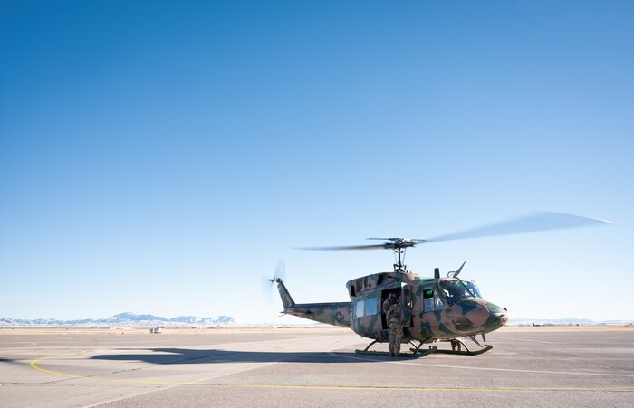 A helicopter sits on a flightline with mountain range faintly visible in the background.