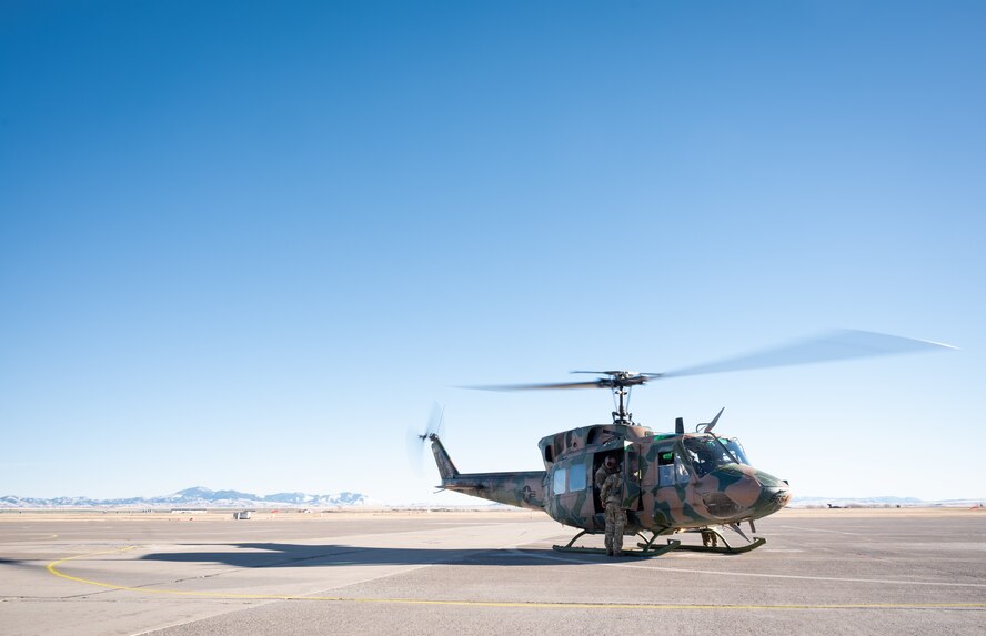 A helicopter sits on a flightline with mountain range faintly visible in the background.